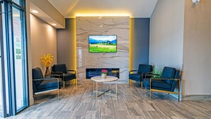 A modern lobby with a marble wall, a flat-screen TV, and two sofas. - Slumber Inn (New Minas)