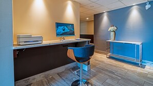 A reception area with a counter, a computer monitor, a blue chair, and a vase with flowers. - Slumber Inn (New Minas)