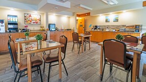 A modern restaurant with a central dining area, a counter with a beverage dispenser, and a kitchen in the background. - Slumber Inn (New Minas)
