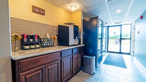 A coffee bar with a sign, a refrigerator, and a trash can in a hallway. - Slumber Inn (New Minas)
