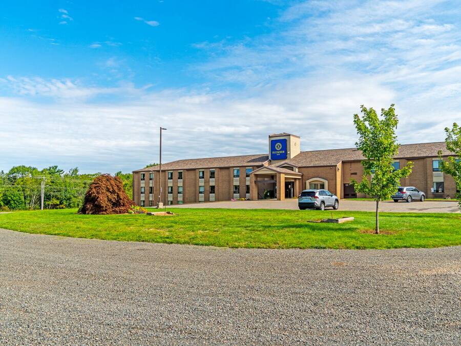 A building with a sign reading "SLUMBER" on the roof, a parking lot with cars, and a grassy area in front.