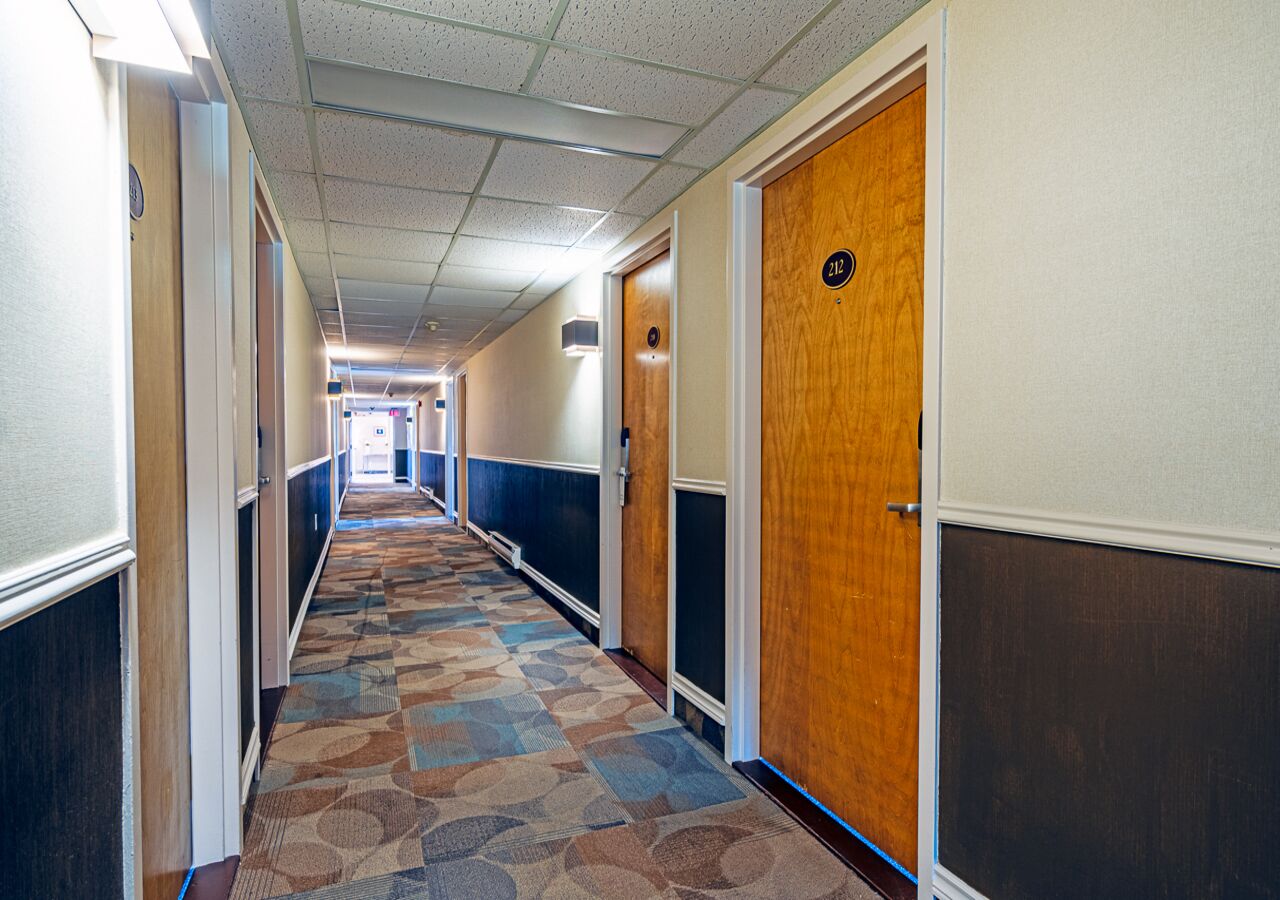 Een hotelgang met een kamergestreept tapijt, houten deuren en een gang naar een kamer.