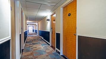 Een hotelgang met een kamergestreept tapijt, houten deuren en een gang naar een kamer.