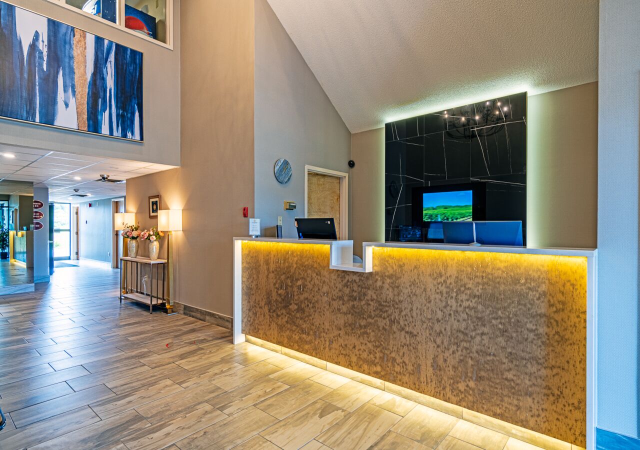 A hotel reception area with a wooden reception desk, a mounted television, and a large abstract painting on the wall.