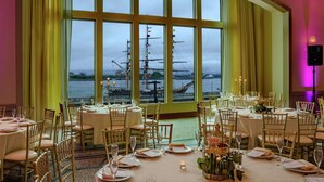 A dining area with tables set for a meal, large windows with curtains, and a view of a ship and water. - Hilton Philadelphia at Penn's Landing (Philadelphia)