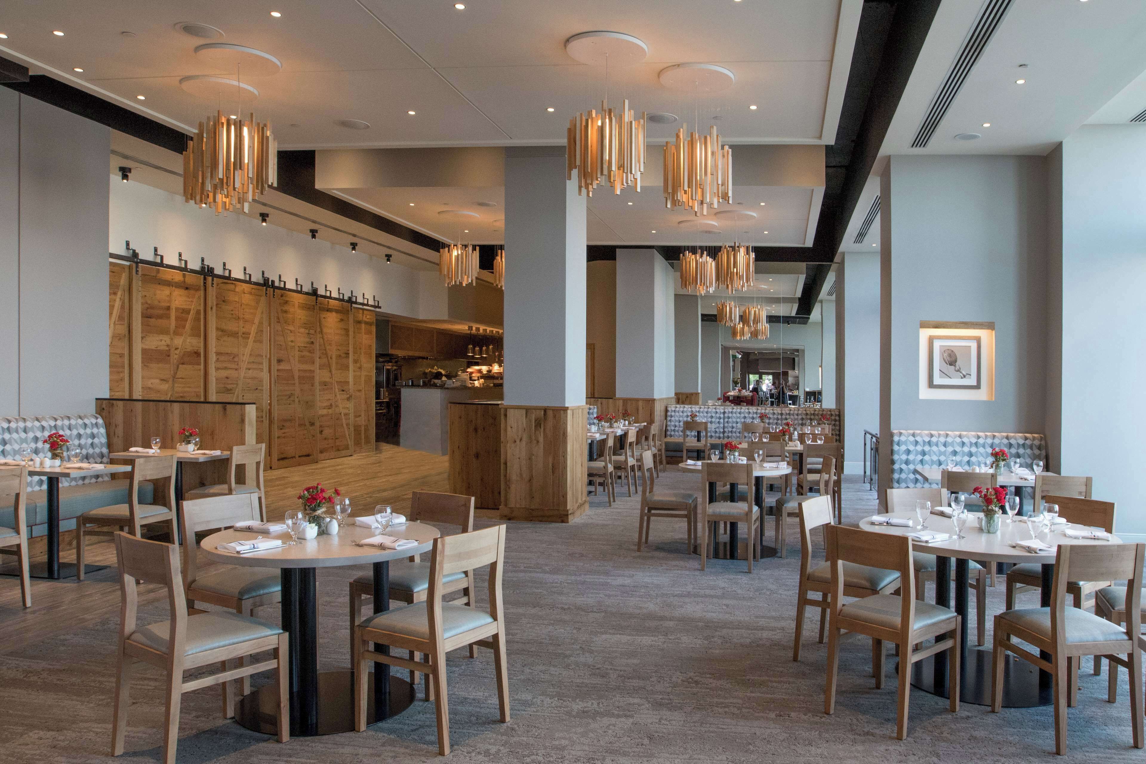 En moderne restaurant med runde borde og træstole, komplet med hængende lamper og et centralt barområde.