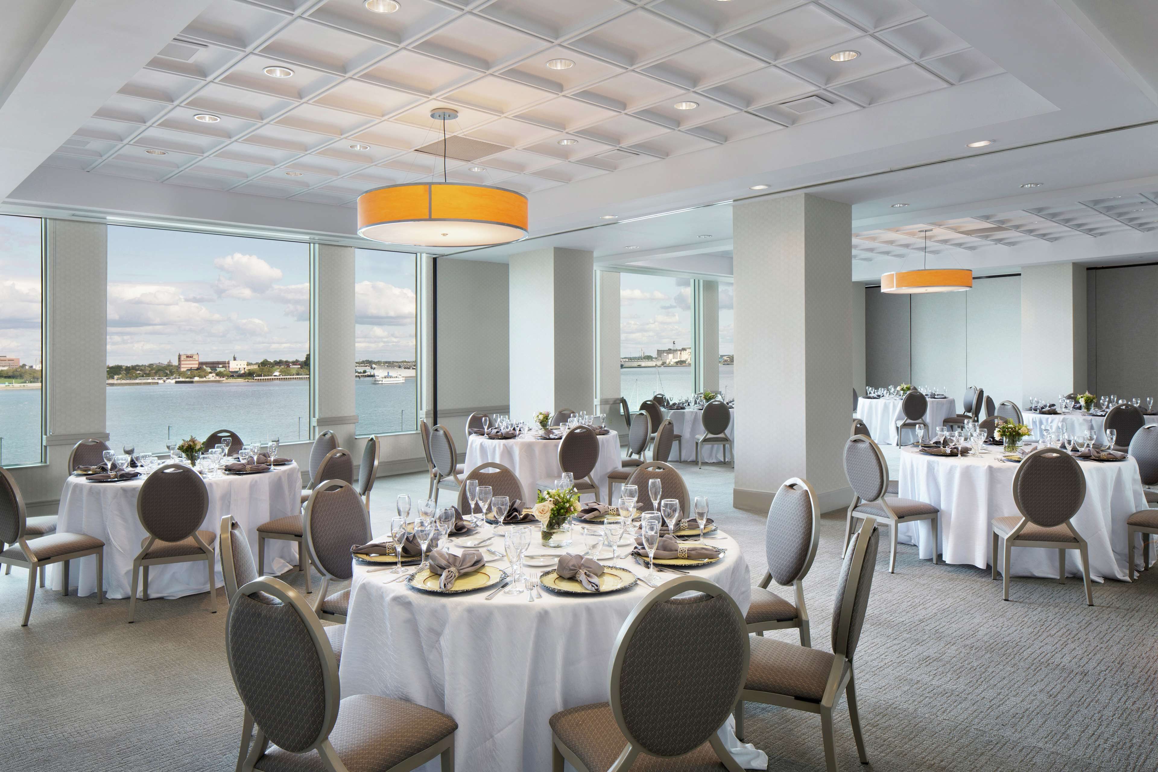 A dining area with round tables set for a meal, large windows, and a view of the water.