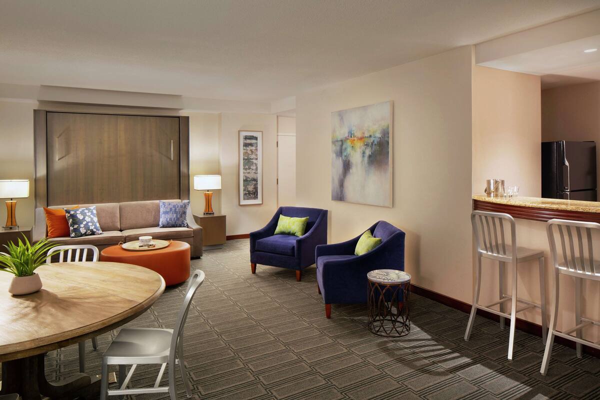 Une chambre d’hôtel moderne équipée d’un canapé, de deux fauteuils, d’une table à manger et d’un coin cuisine.
