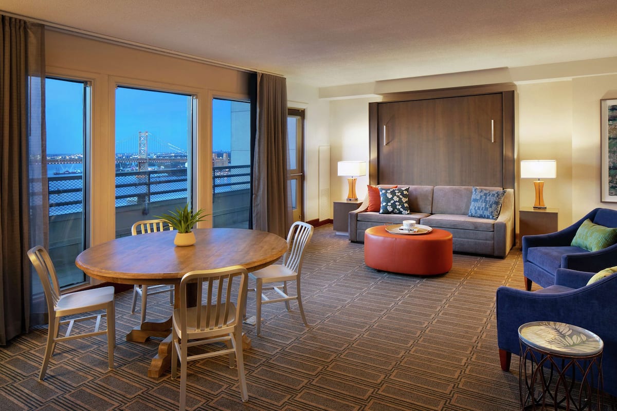 Une chambre d’hôtel avec un balcon, un coin repas comprenant une table et des chaises, un canapé et un fauteuil bleu.