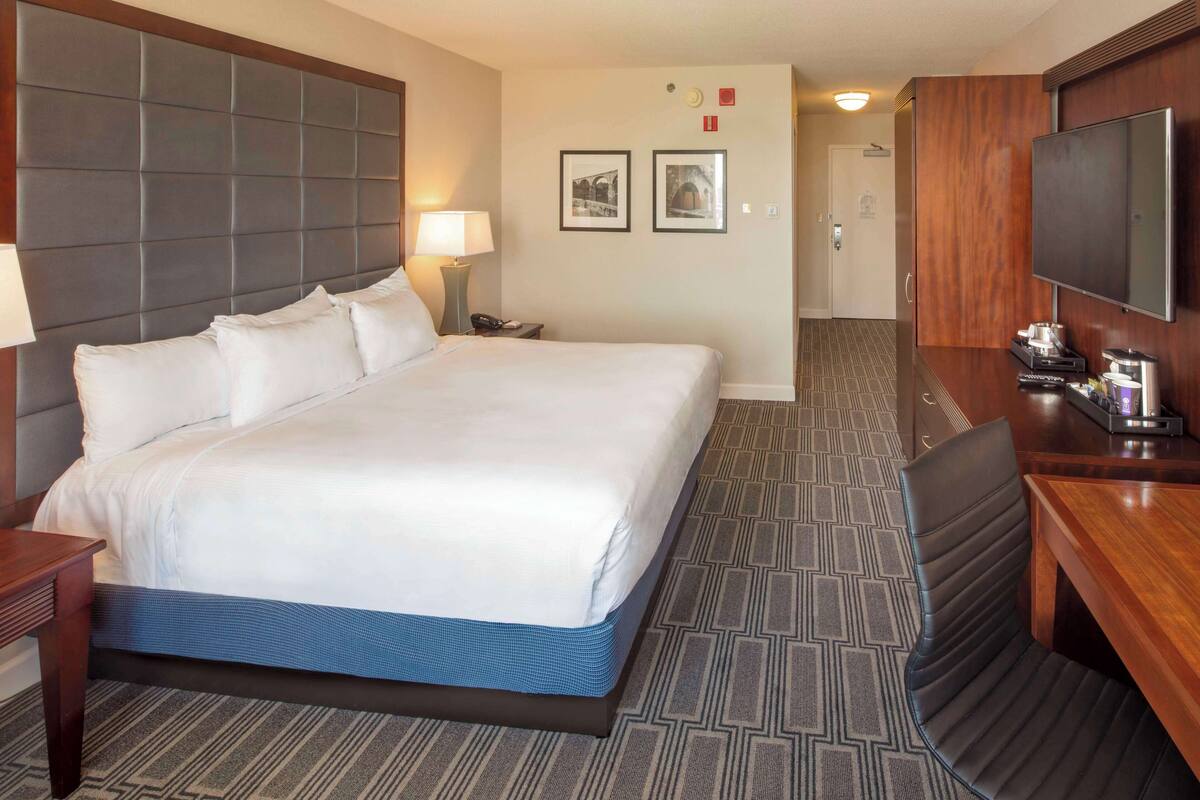 Une chambre d’hôtel avec un grand lit, un bureau doté d’un téléviseur à écran plat, une lampe et une machine à café.