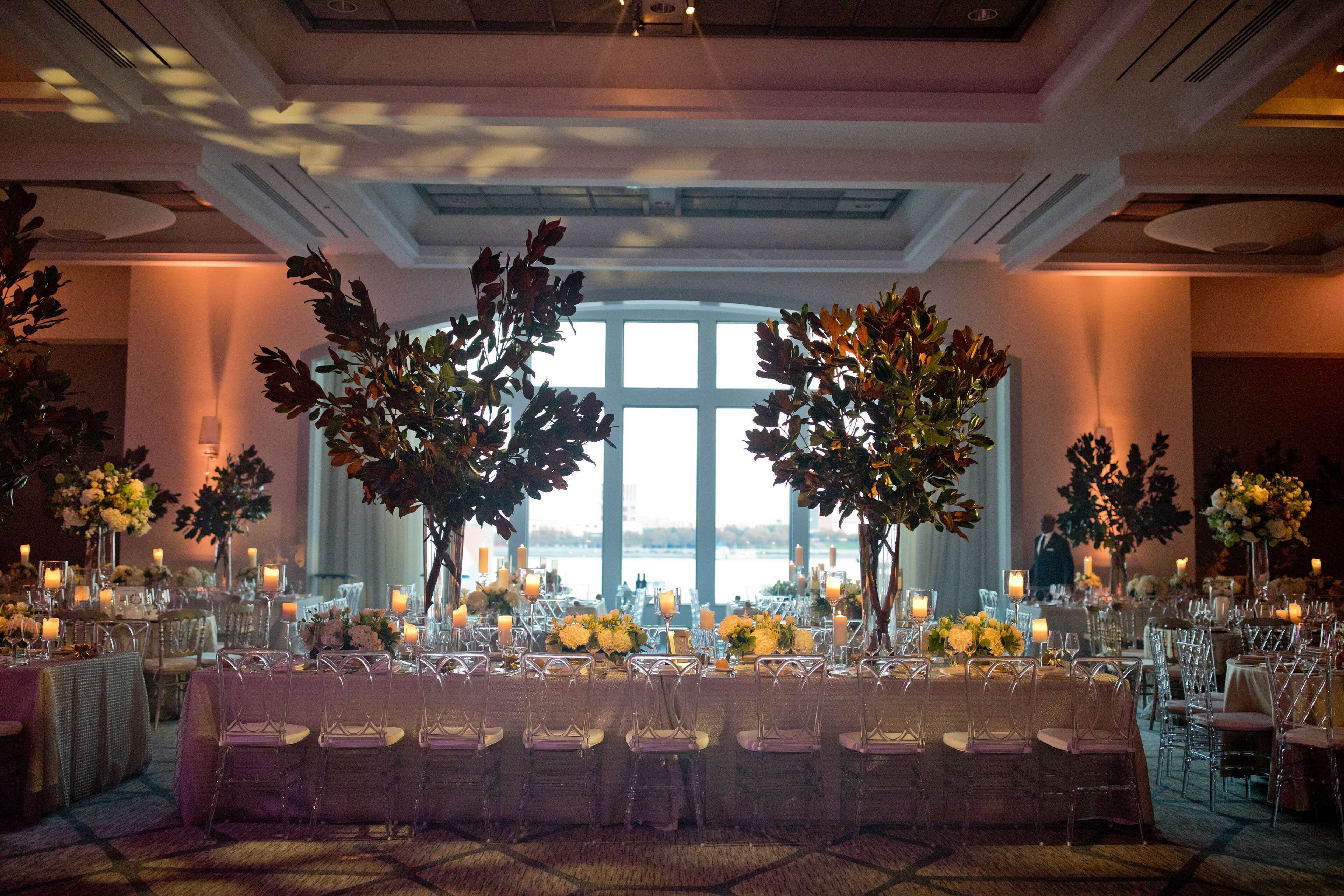 A banquet hall with long tables, clear chairs, and floral centerpieces.