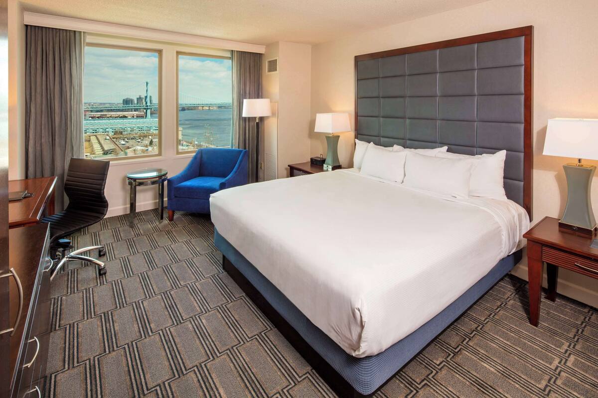 Une chambre d’hôtel avec un grand lit, un bureau, une chaise et une vue sur un pont et sur l’eau.