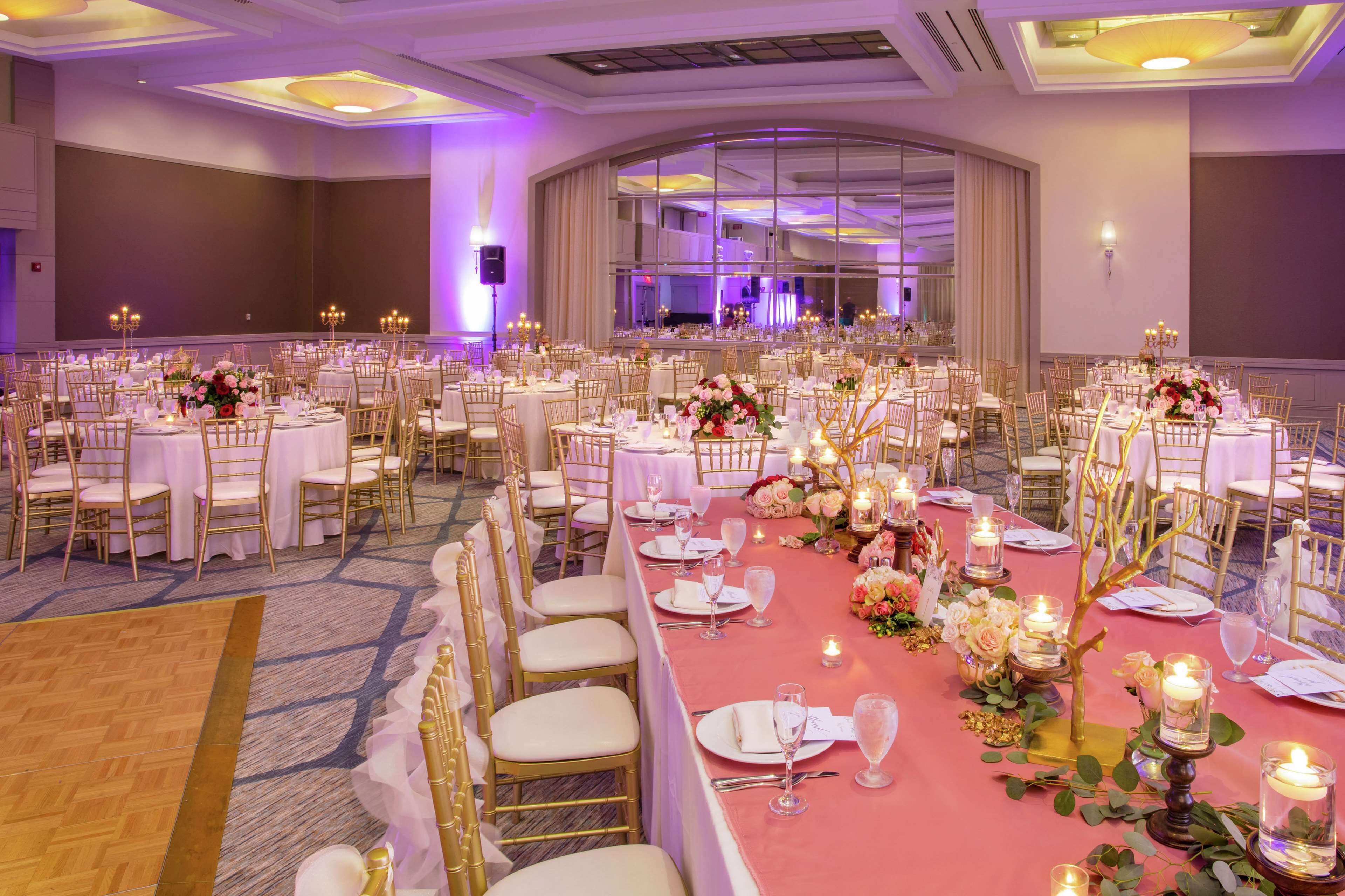 Un salón de banquetes con mesas redondas, manteles blancos y sillas doradas.