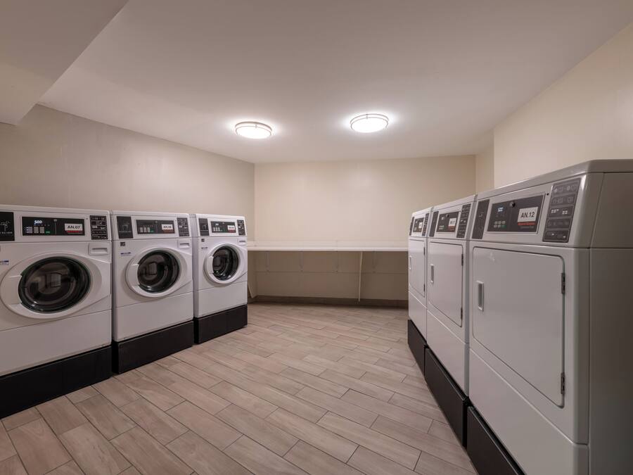 Een wasserette met meerdere wasmachines en drogers, een betegelde vloer en een wit plafond met inbouwverlichting.