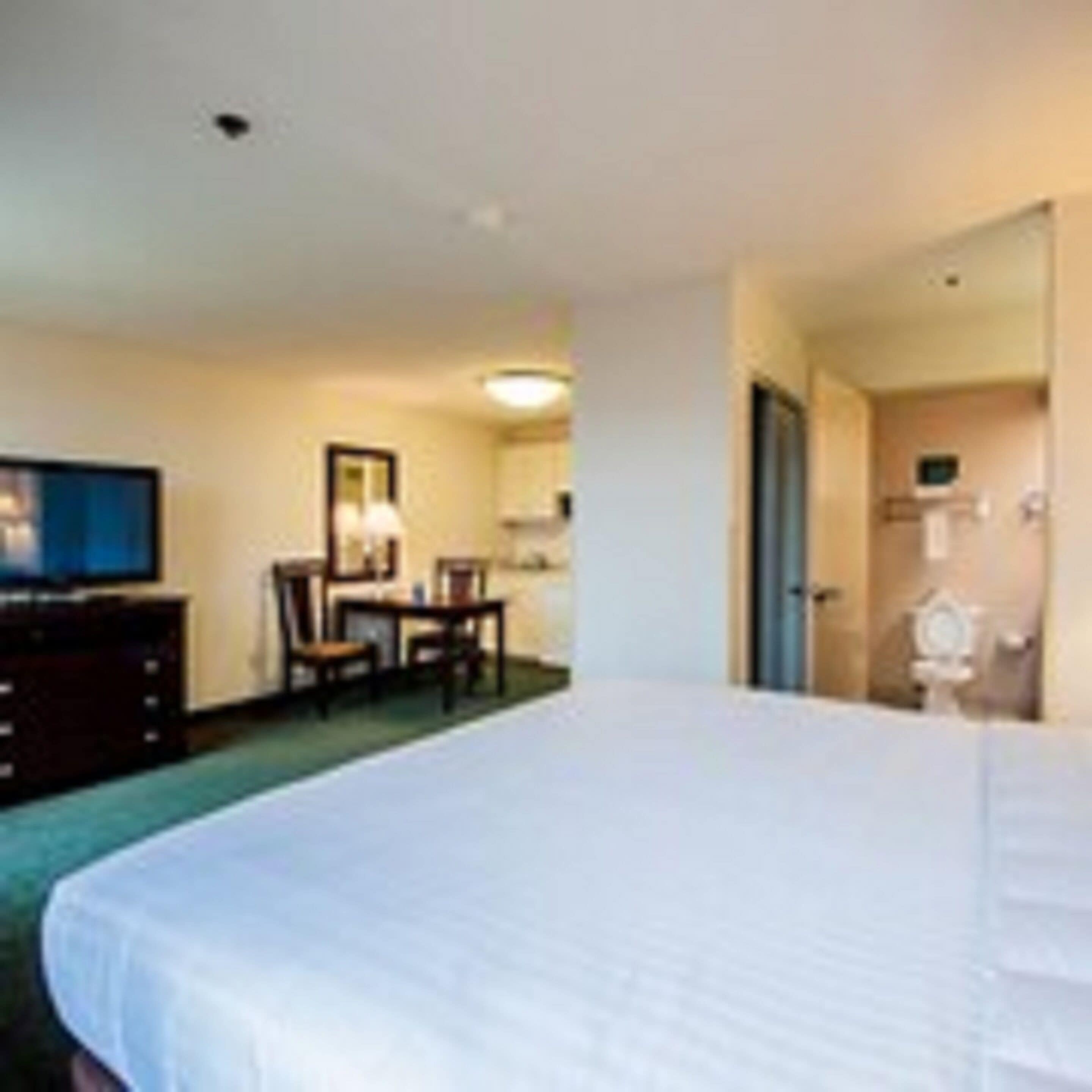 Une chambre d’hôtel avec un grand lit, un bureau avec une chaise, une télévision et une salle de bain visible à travers une porte ouverte.