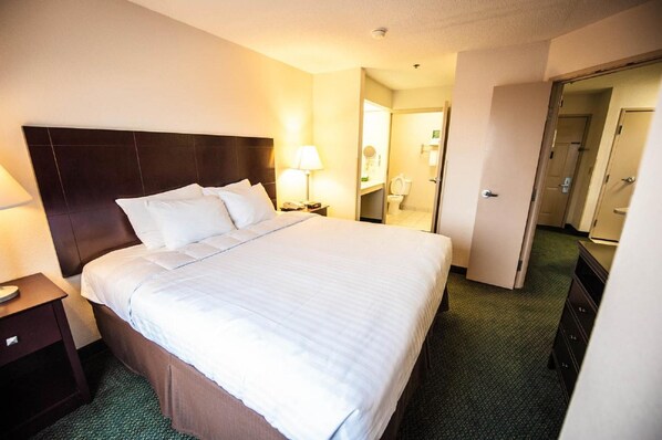 A hotel room with a bed, a nightstand, a lamp, and a bathroom visible through an open door.