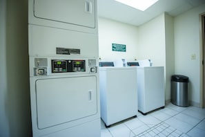 A laundry area with two washing machines and a trash bin. - Greystone Inn and Suites (Vance)