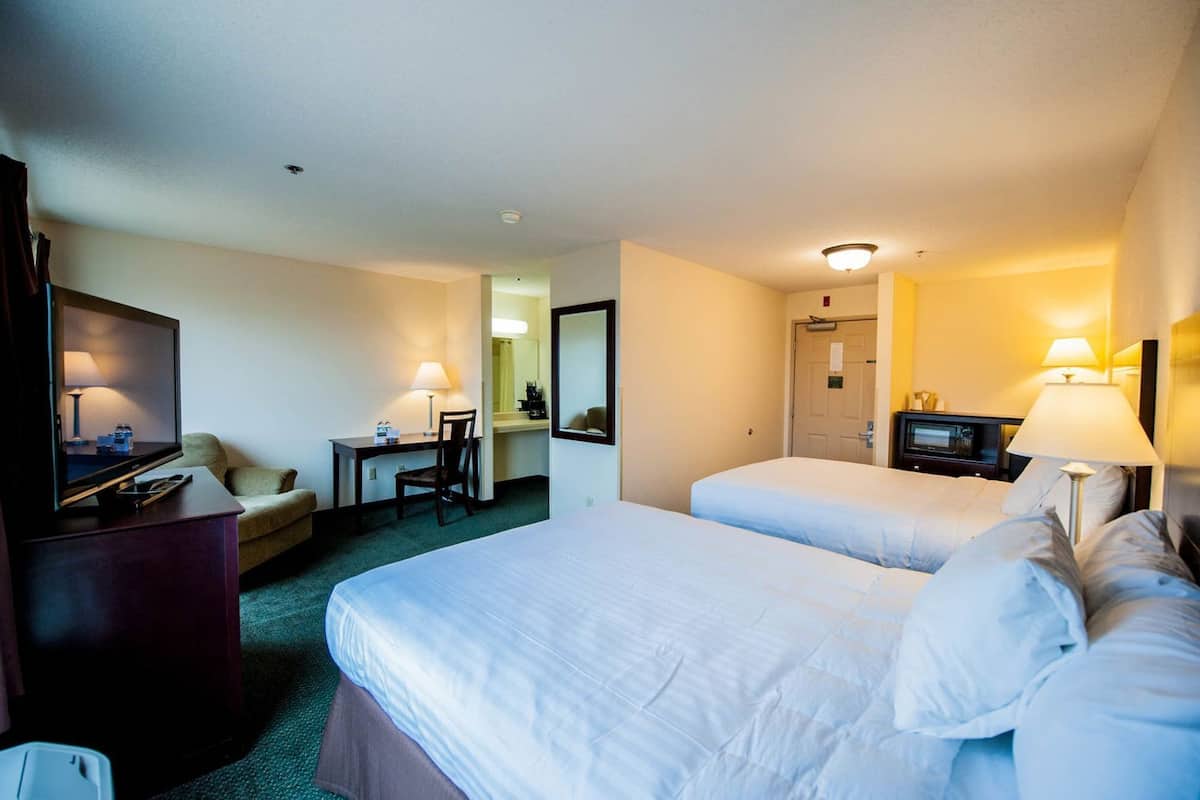 A hotel room with two beds, a desk with a chair, a television, and a mirror.