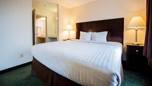 A hotel room with a large bed, two bedside tables with lamps, a dark headboard, and a door leading to a bathroom.