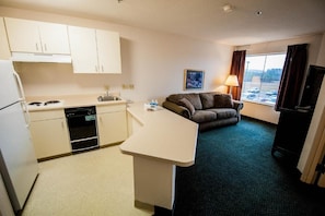 Habitación de hotel compacta con kitchenette, sofá, televisión y ventana con vista a coches estacionados.