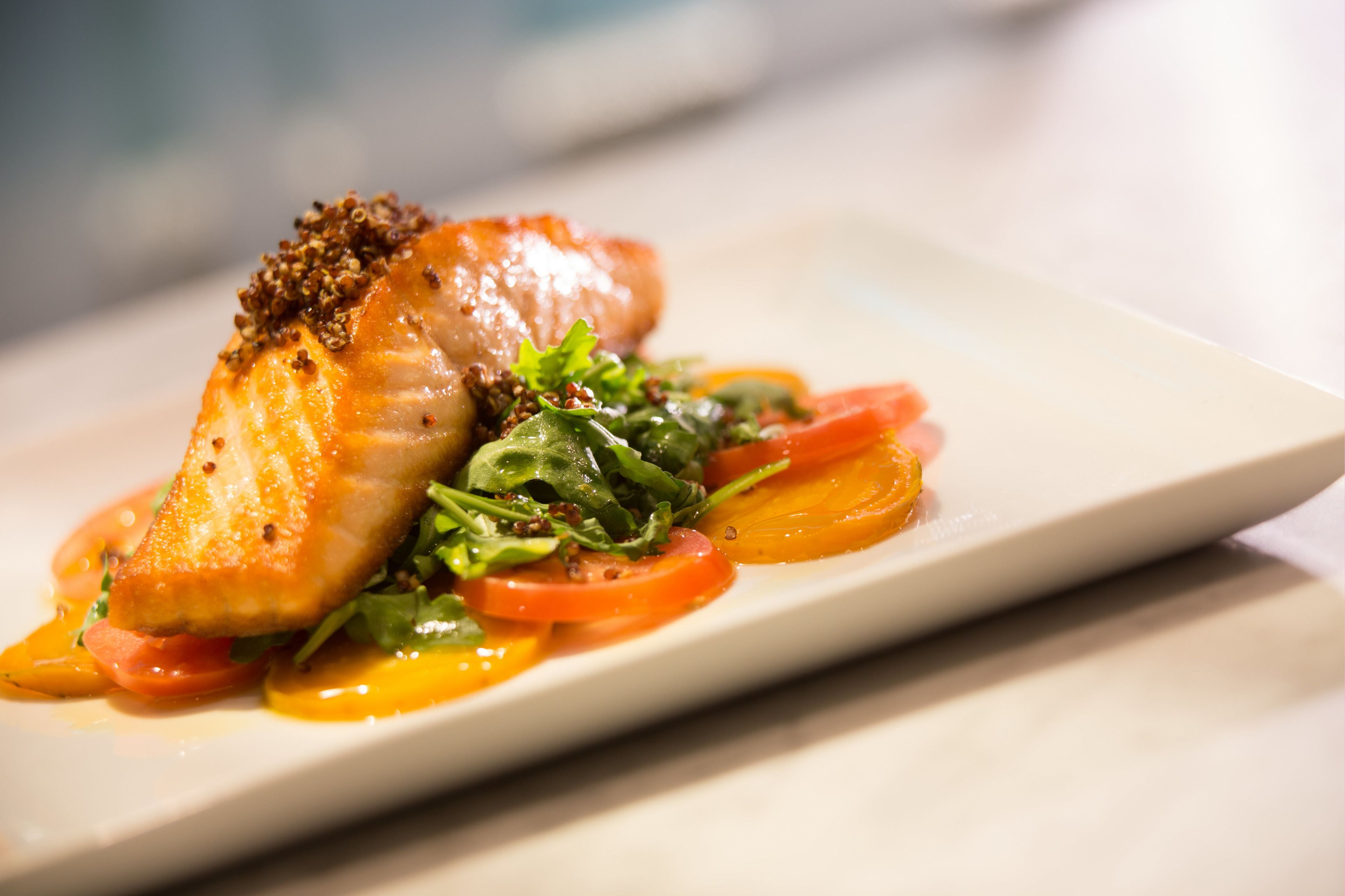 A plate with a piece of salmon, cherry tomatoes, and greens.