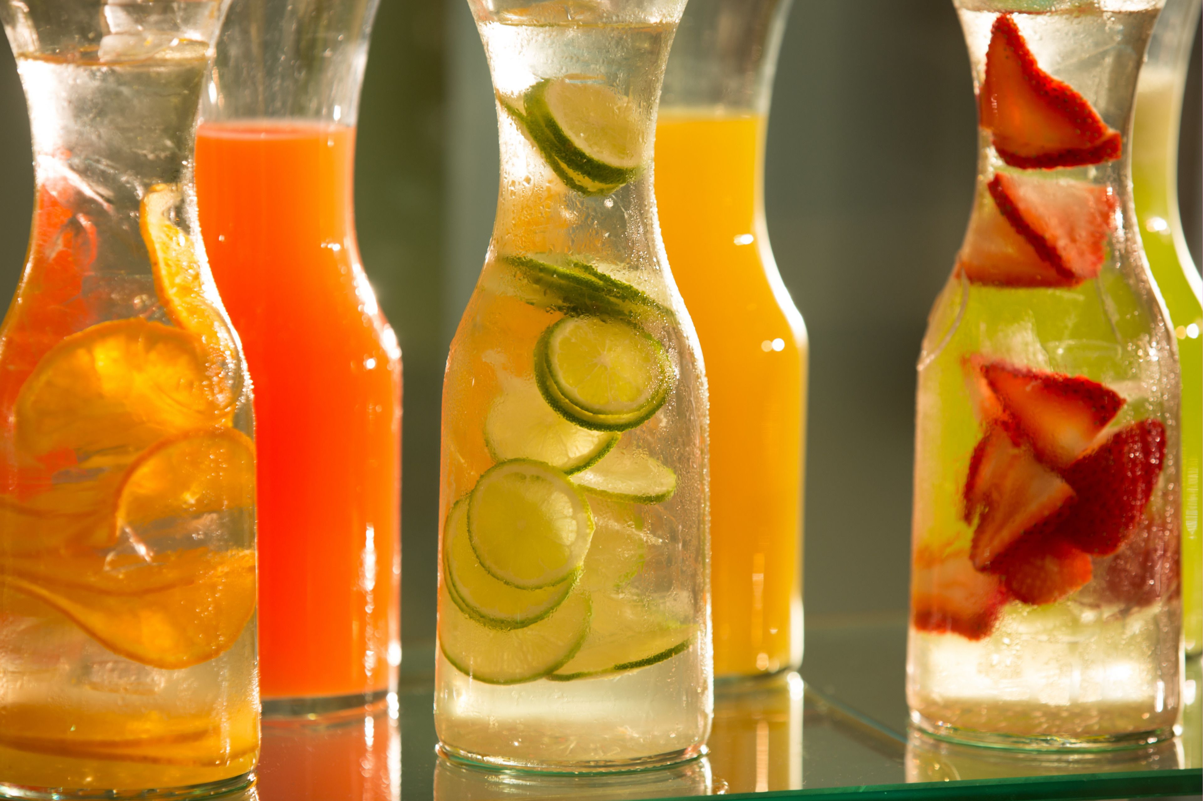A row of clear glass bottles with different colored liquids and slices of lime and strawberries.