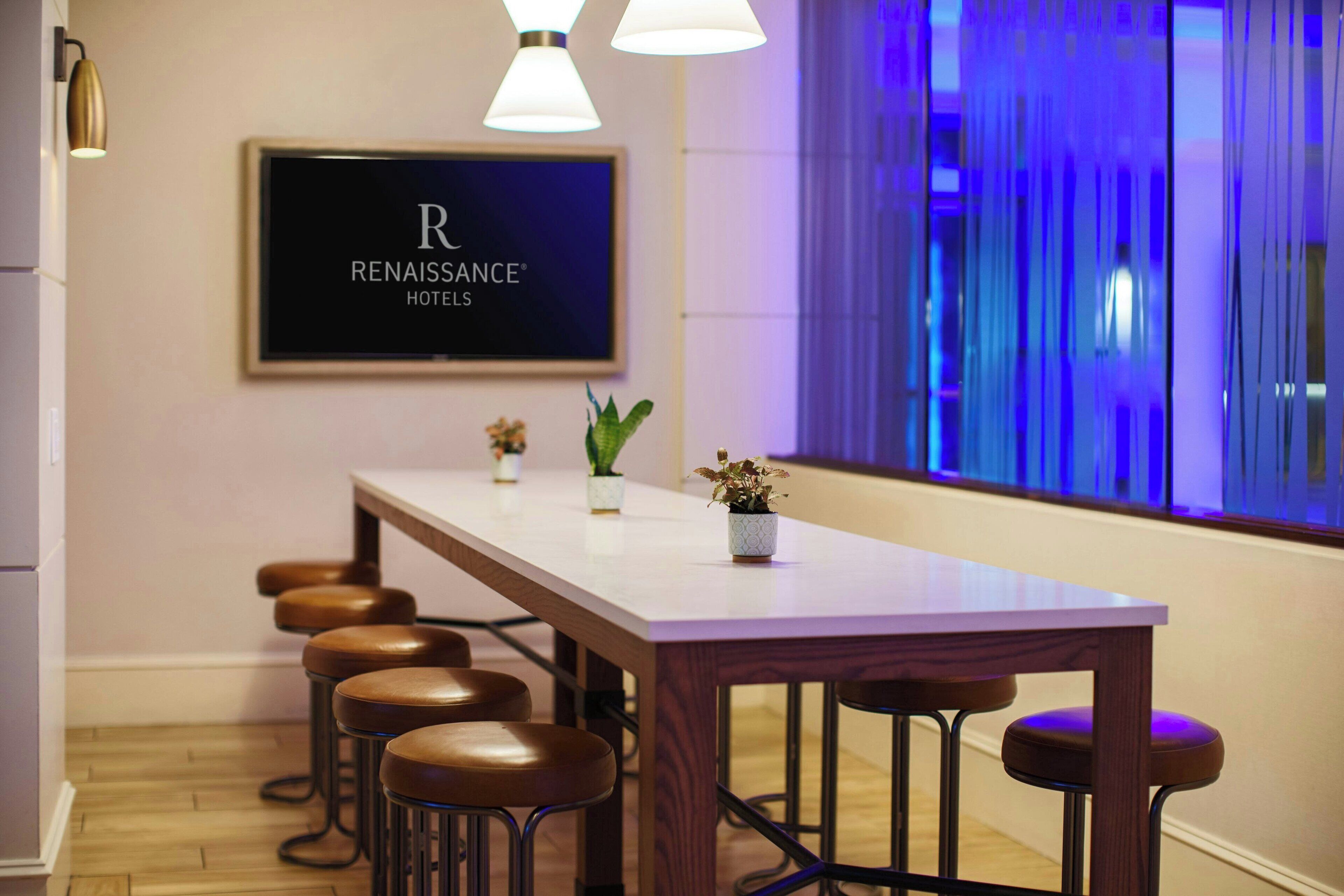 A conference table with four stools, a potted plant, and a framed sign for Renaissance Hotels.