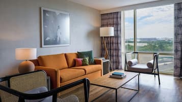 Een moderne hotelkamer met een bank, twee stoelen, een bijzettafeltje en een groot raam met uitzicht op de stad.