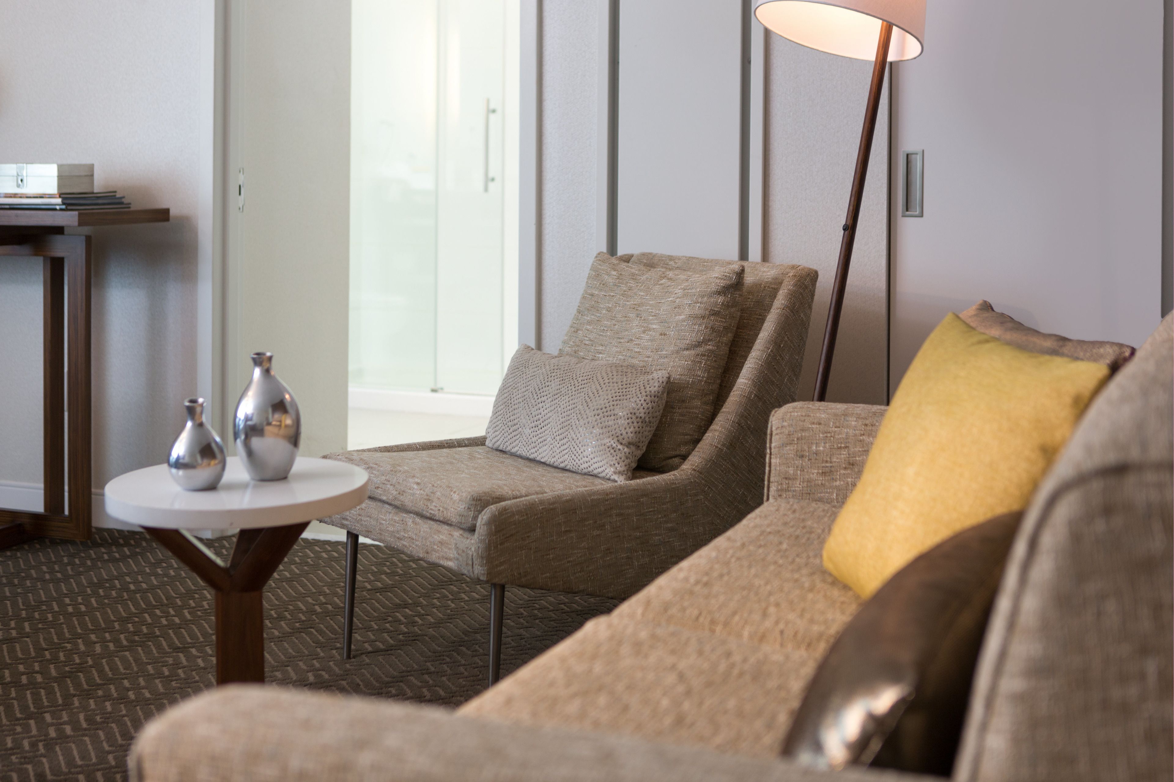 A modern living room with a sofa, armchair, and a small round table with decorative vases.