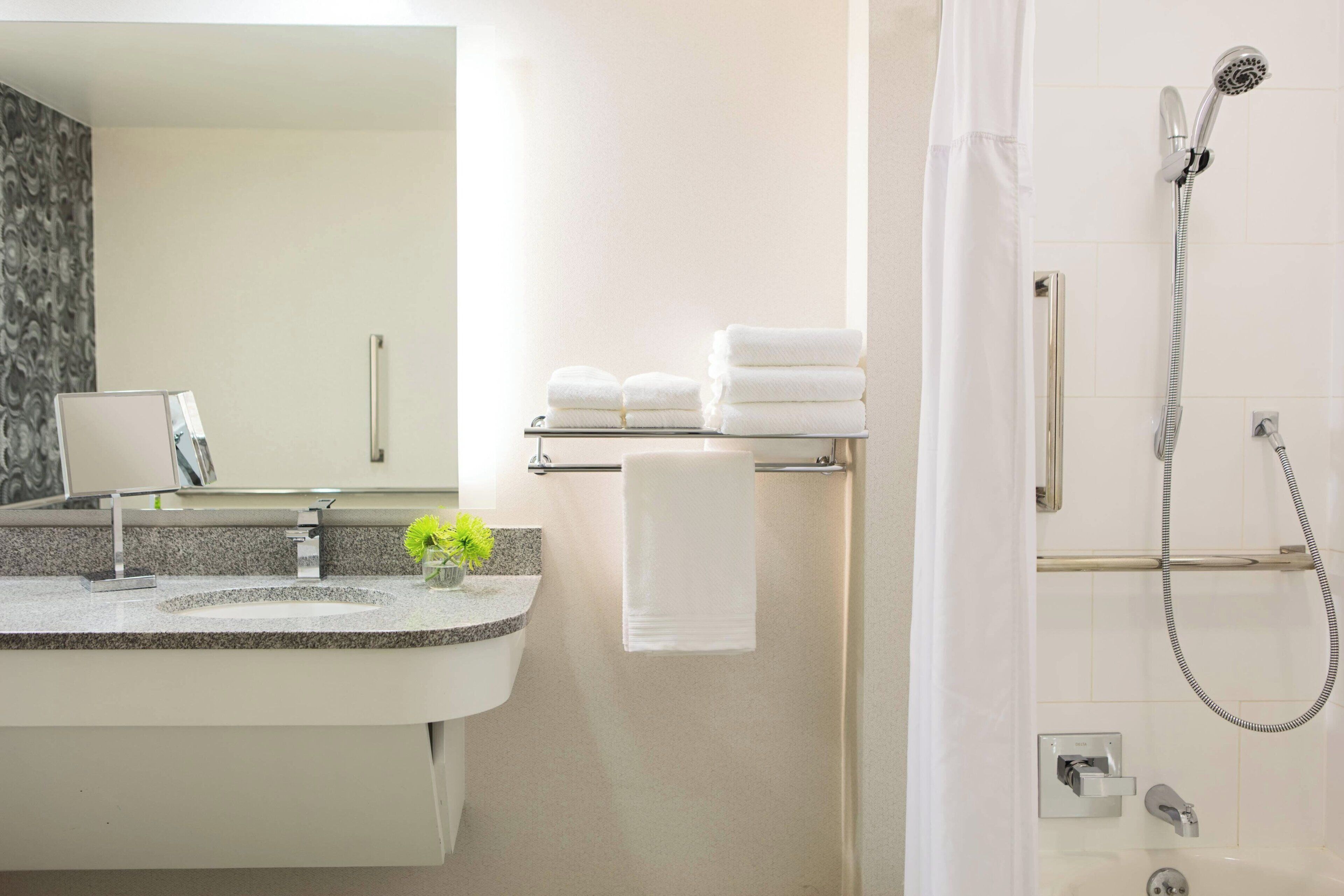Un baño moderno con lavamanos de granito, un espejo, un perchero con toallas dobladas y una ducha con cabezal de ducha de mano.