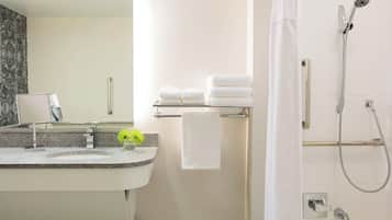Un baño moderno con lavamanos de granito, un espejo, un perchero con toallas dobladas y una ducha con cabezal de ducha de mano.
