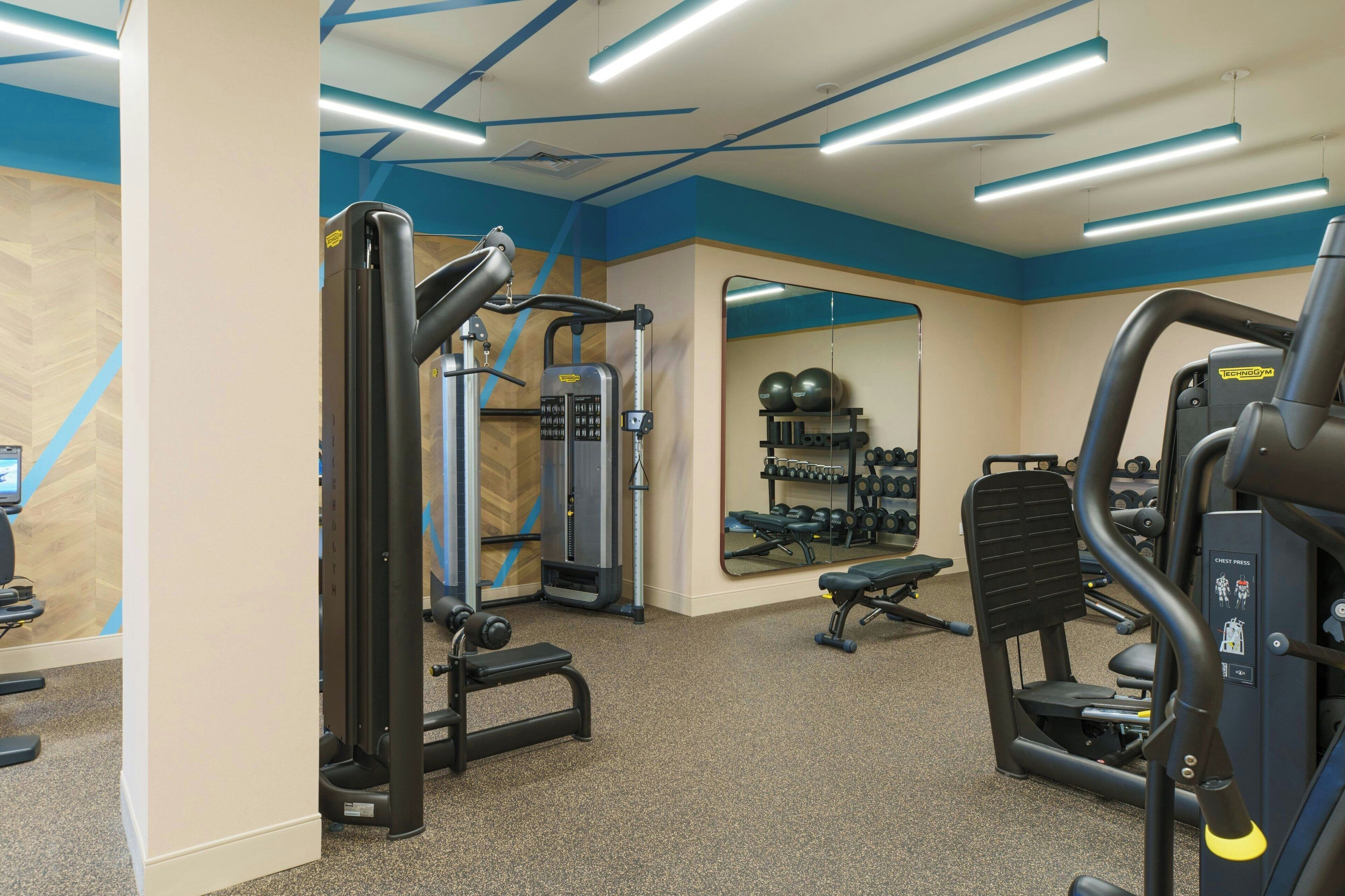 A gym with various exercise machines, a mirrored wall, and a weight rack.