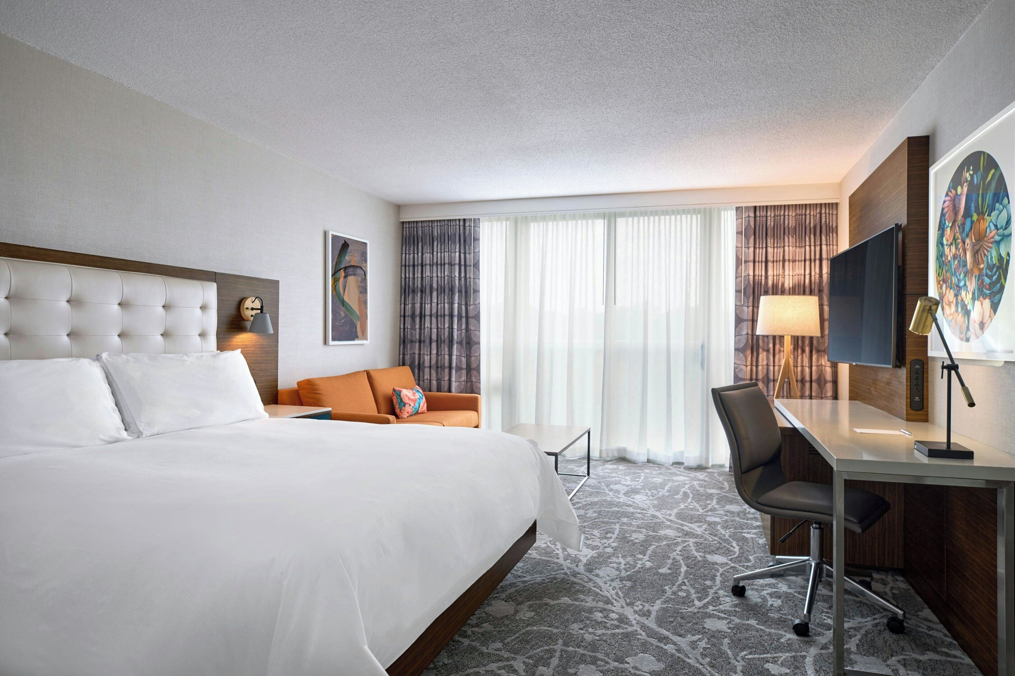 A hotel room with a large bed, a desk, a chair, and a television.