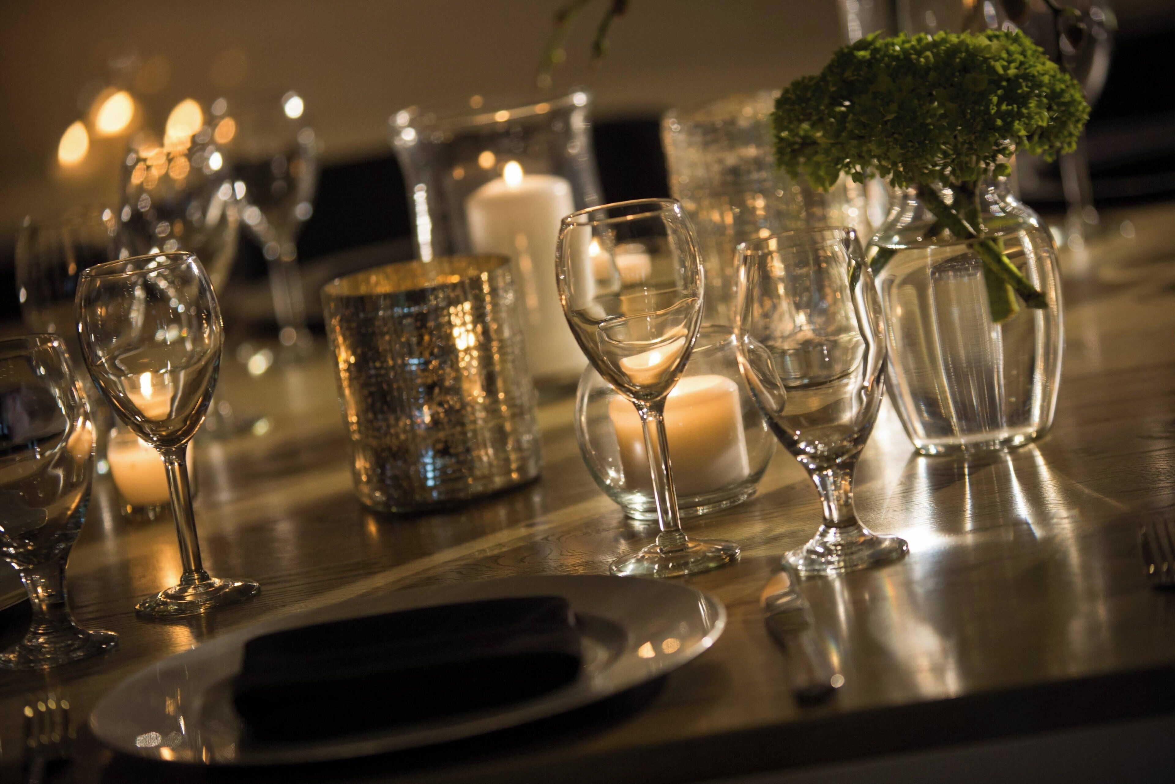 A table set with wine glasses, a candle, and a decorative vase with greenery.