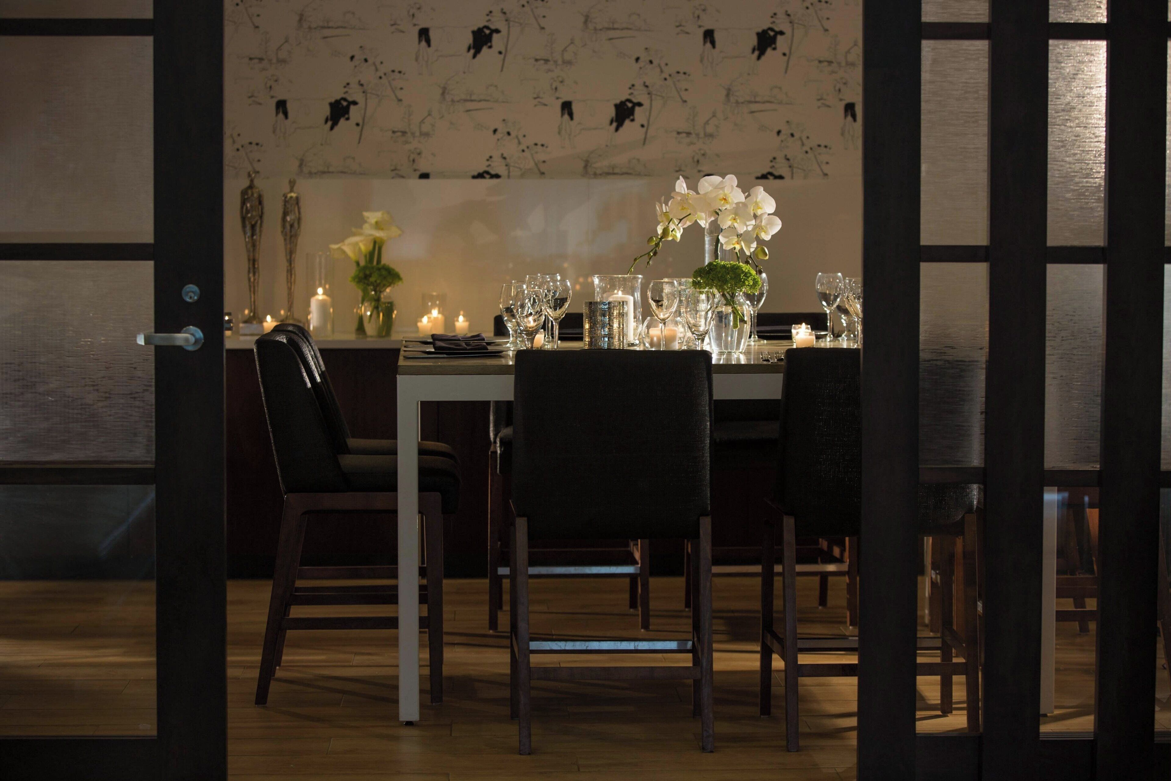 Un coin repas avec une table mise pour quatre personnes, des chaises, des bougies et un vase rempli de fleurs.