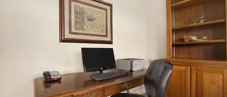 A wooden desk with a computer, a telephone, and a framed picture on the wall.