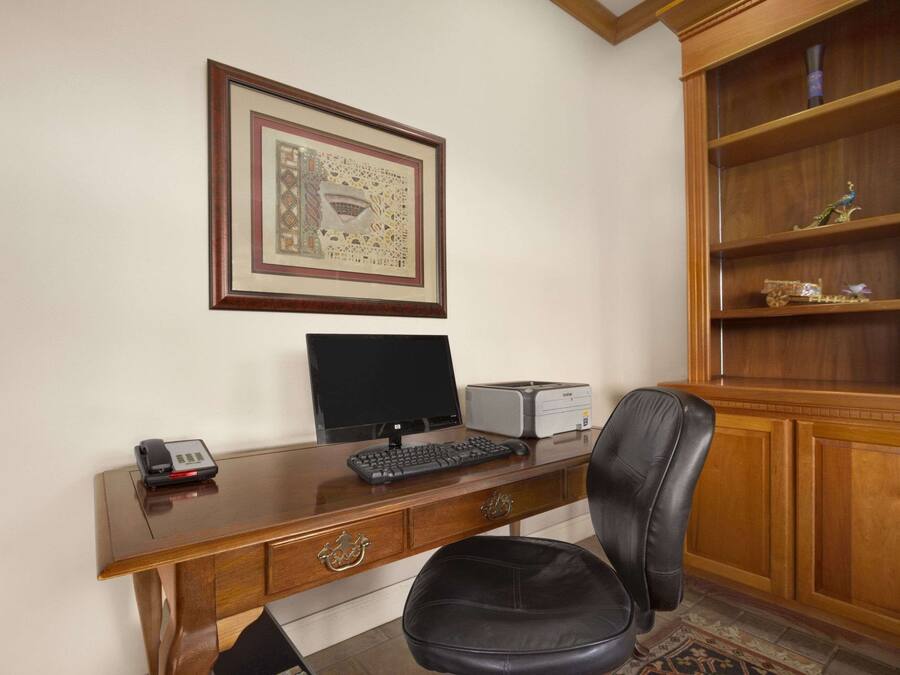 A wooden desk with a computer, a telephone, and a framed picture on the wall.