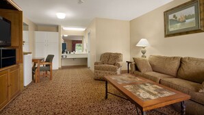 A living room with a sofa, armchair, and coffee table. There is a television, a lamp, and a painting on the wall. - Days Inn by Wyndham Alexander City (Alexander City)