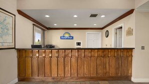 A reception desk with a Days Inn sign, wooden paneling, a clock, and a framed map on the wall. - Days Inn by Wyndham Alexander City (Alexander City)