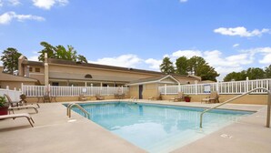 A swimming pool with lounge chairs and a fence, surrounded by a building with a beige exterior. - Days Inn by Wyndham Alexander City (Alexander City)