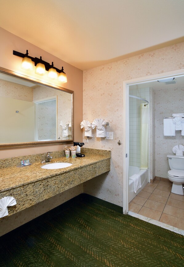 A bathroom with a granite countertop sink, a large mirror, a shower with a glass door, and a toilet. - Lamplighter Inn & Suites at SDSU (San Diego)