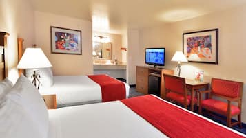 A hotel room with two beds, a desk with a computer, a chair, a lamp, and artwork on the walls.