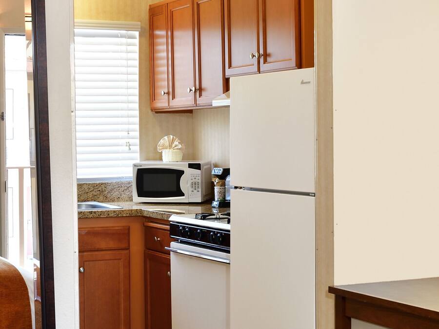 A compact kitchen with wooden cabinets, a white refrigerator, a microwave, and an oven.