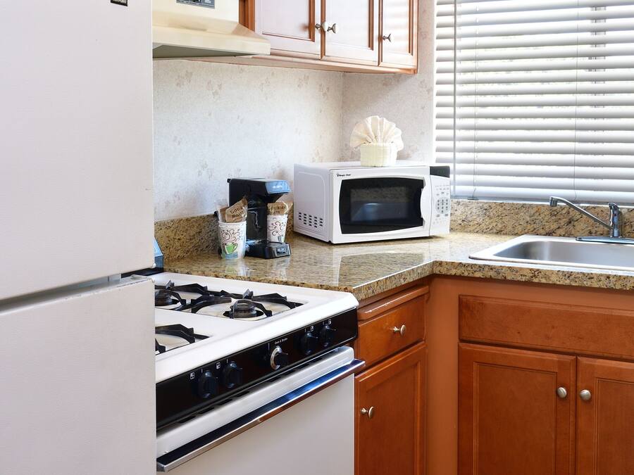 A kitchen with wooden cabinets, a gas stove, a microwave, and a sink.