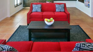 Un vaste espace de vie agrémenté d’un canapé rouge, d’une table basse sur laquelle est posé un panier de fruits et d’un lustre moderne.