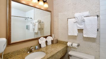 A bathroom with a granite countertop, a sink, a toilet, a mirror with lights, and towels on a rack.
