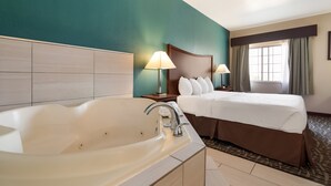 A hotel room with a large bathtub, a neatly made bed with white linens, and a teal-colored wall. - SureStay Plus Hotel by Best Western Topeka Northwest (Topeka)