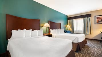 A hotel room with two beds, a desk, a chair, a lamp, and a window with curtains.