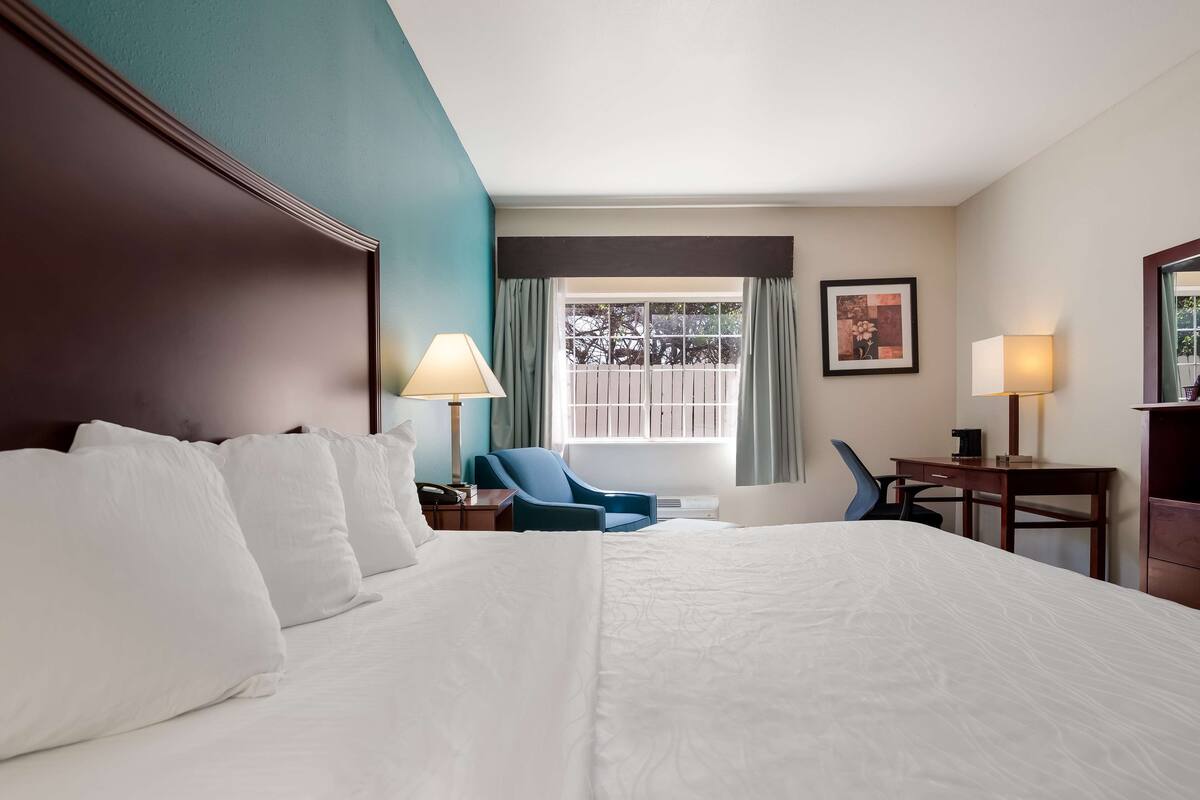 A hotel room with a large bed, a desk, a chair, and a window with curtains.