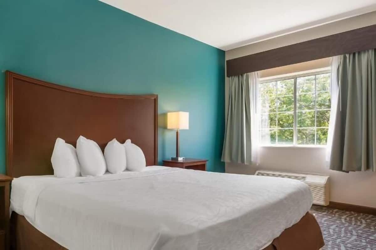 A hotel room with a large bed, two bedside tables, a window with curtains, and teal walls.